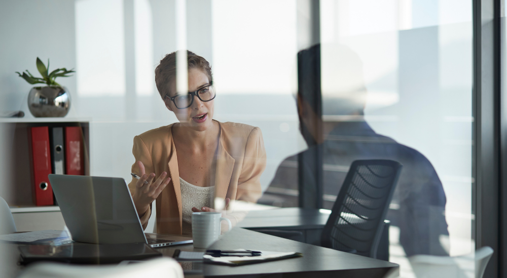 Woman and man discussing insurance over a laptop viewed through a glass window